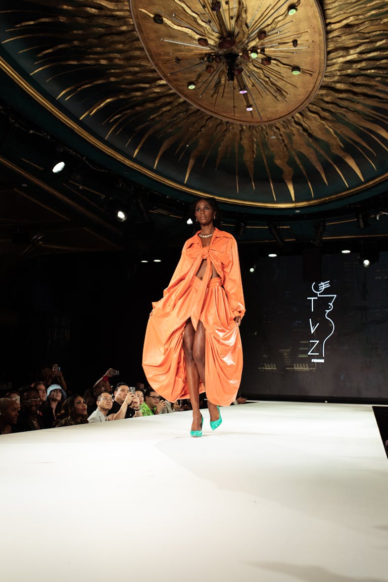 Elegant fashion model on runway flaunting an orange designer outfit at high-profile show.